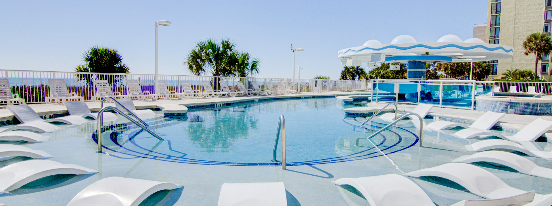 A large outdoor pool with a beach and palm trees in the background.