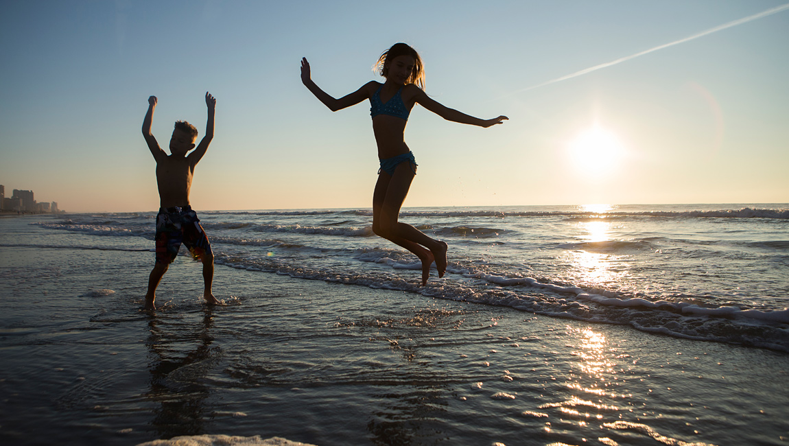 Two children playing in the waves at the beach during sunset.