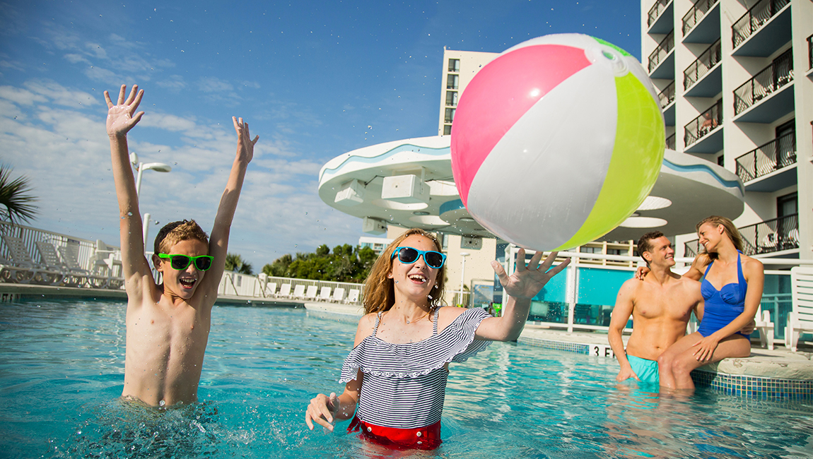 A family of four enjoys a playful moment in the hotel pool with a large beach ball.