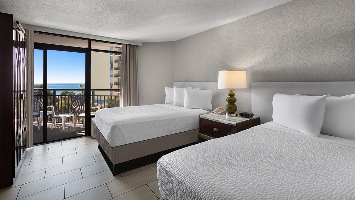 A hotel room with two double beds, a balcony, and a view of the ocean.