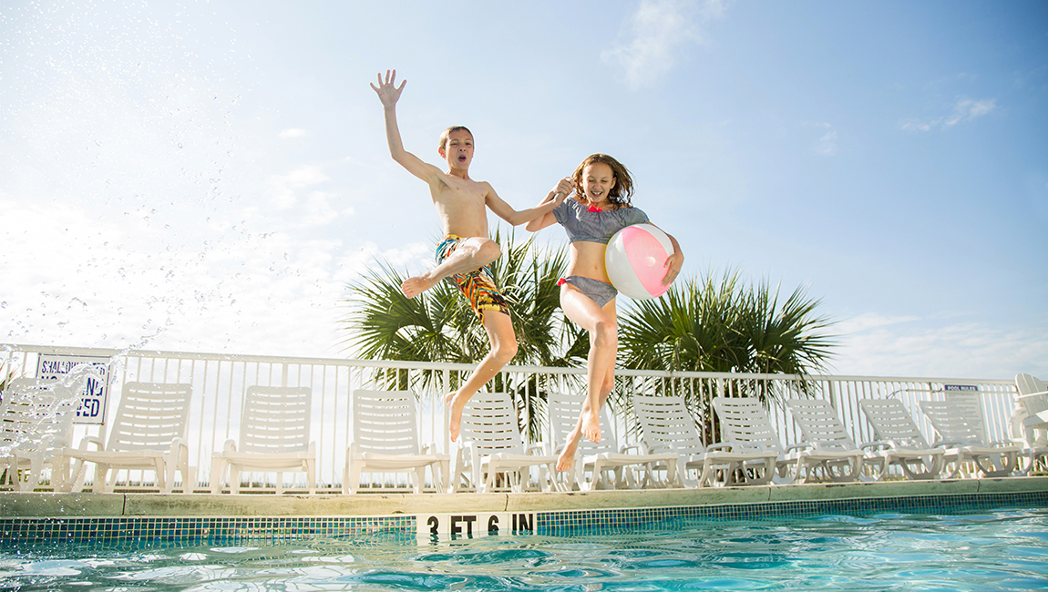 Two children jumping into a pool on a sunny day