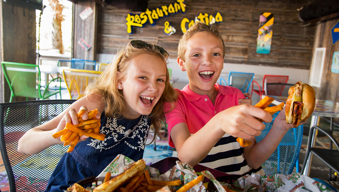 Two children sitting at a table with food in a restaurant.