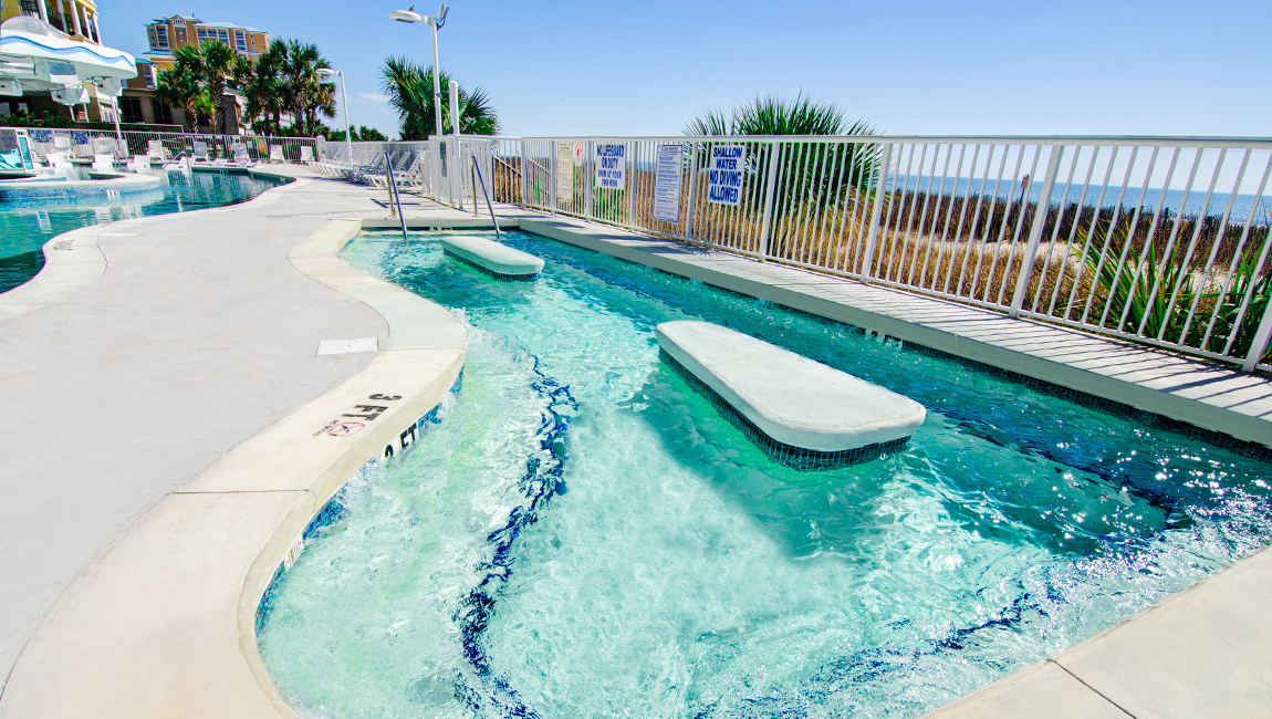 A swimming pool with a curved edge and steps leading into it, surrounded by white fencing and palm trees.