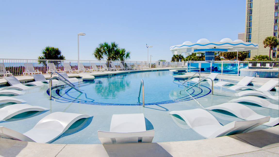 A large pool with white lounge chairs and palm trees in the background.