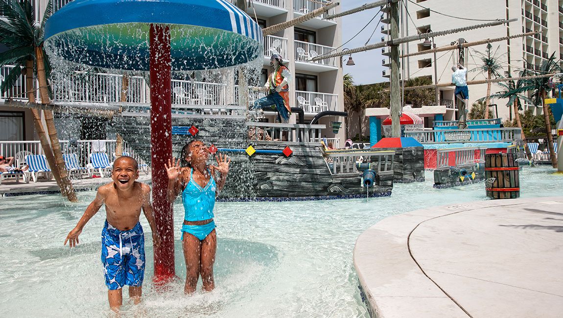 Two children playing in a pool with a water feature.
